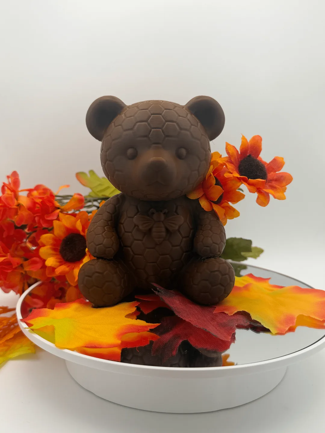 Front view of 3d printed bear figurine on a mirrored stand with orange flowers and fall leaves