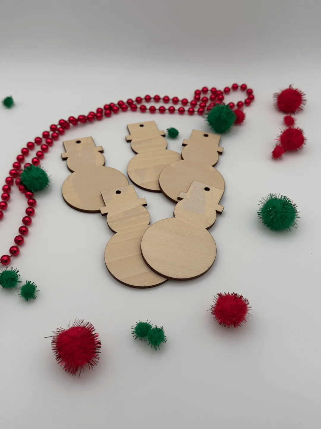 Angled view of unfinished wood snowman ornaments showing birch plywood thickness and pre-drilled holes