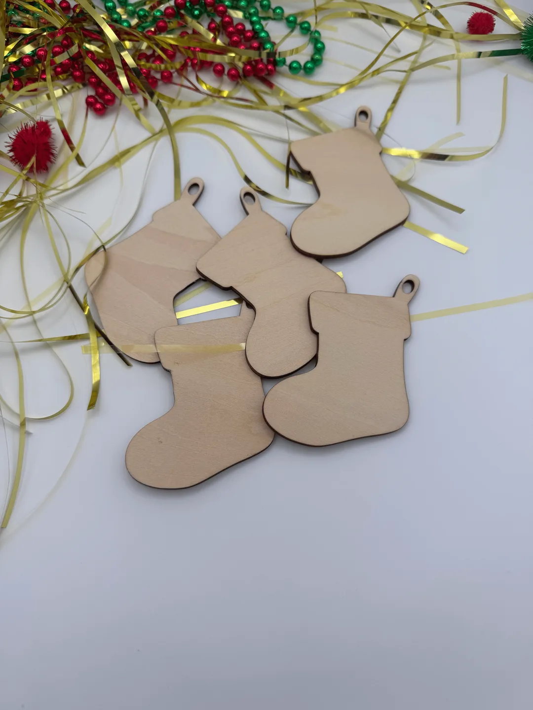 Unfinished wood stocking ornaments arranged together with festive ribbon and Christmas bead garland